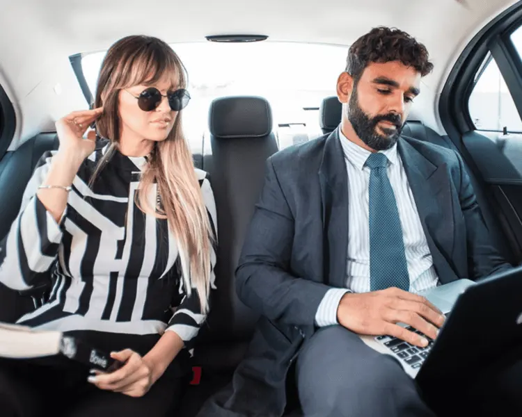 Two business travellers working in the back seat of a chauffeured car