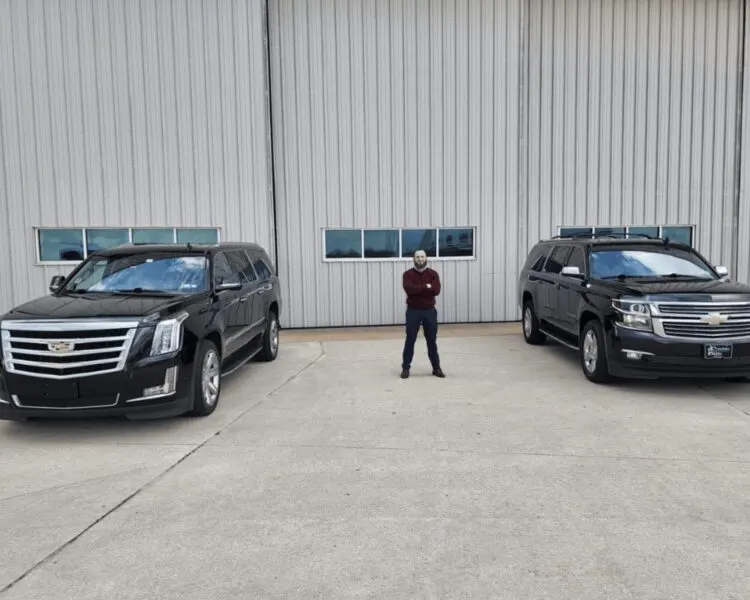 Black Cadillac Escalade ESV and Chevrolet Suburban outside a hangar