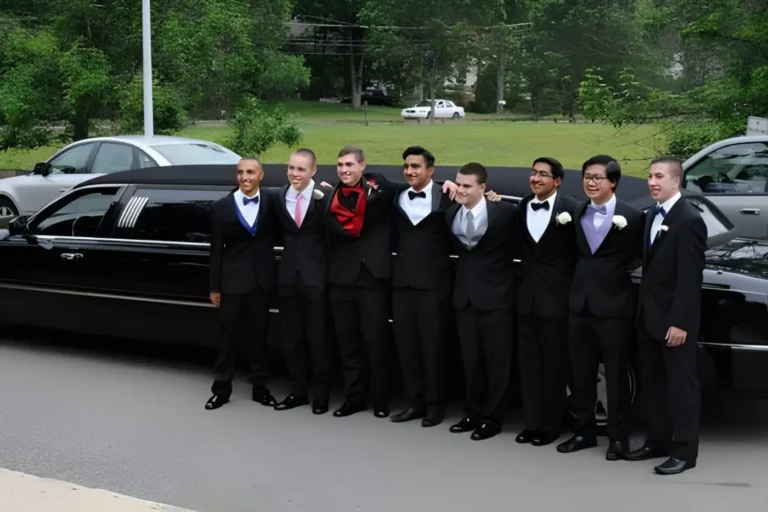 Group of young men in tuxedos lined up beside black cars