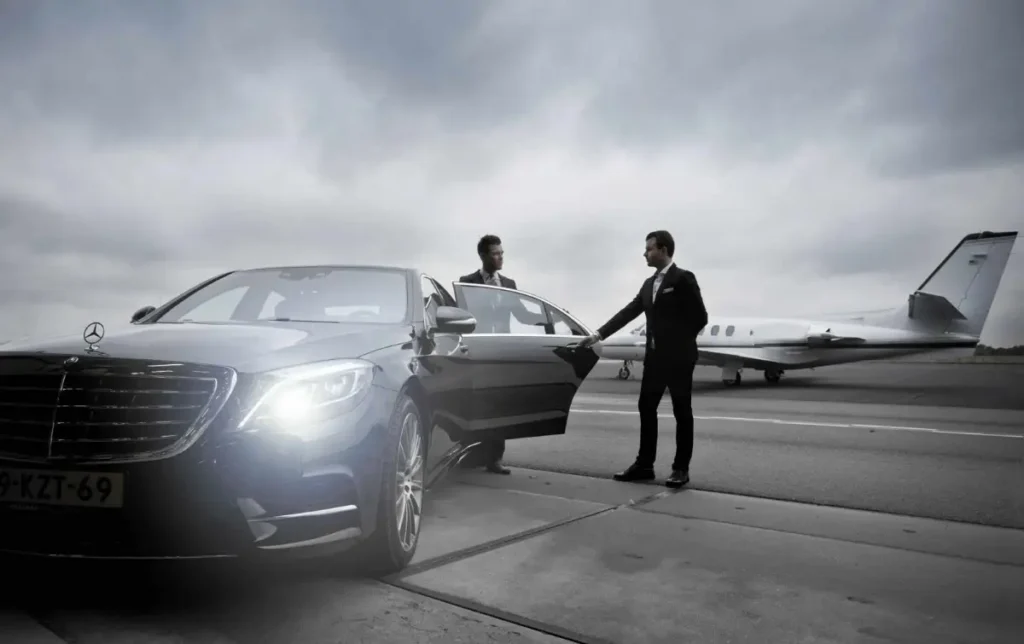 Chauffeur opening the door of a black sedan beside a private jet