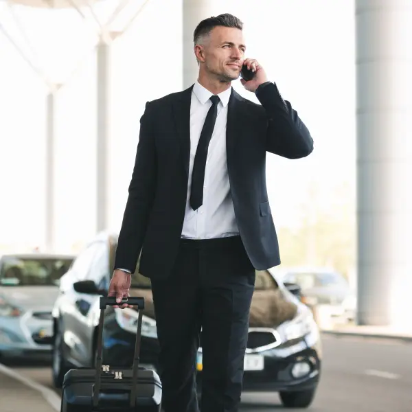 Business traveller on a call beside a waiting chauffeured car